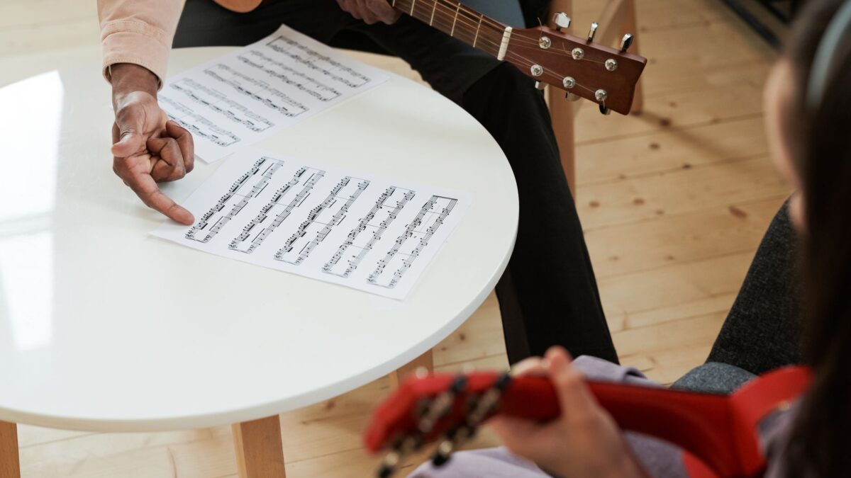 Hände greifen einen Akkord auf einer Gitarre über einem Notenblatt
