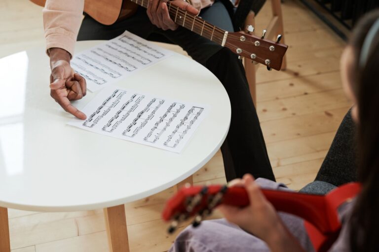 Hände greifen einen Akkord auf einer Gitarre über einem Notenblatt
